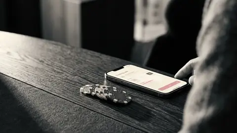 Mobiltelefon med en bankapp bredvid en hög casinomarker på ett mörkt träbord
